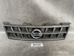 Nissan front grille with circular chrome emblem, black plastic slats, on a textured gray surface.