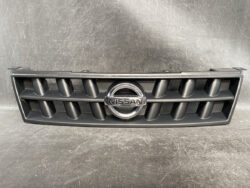 Nissan front grille with a chrome circular emblem in the center on a black plastic frame.