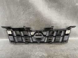 Black plastic front grille panel for a vehicle, featuring hexagonal openings and a central circular emblem mount underway of a logo area in the middle.