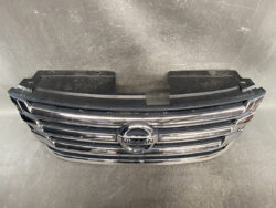 Nissan front grille with chrome horizontal bars and centered circular emblem on a dark bumper piece.