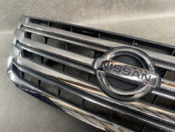 Close-up of a Nissan car grille with horizontal chrome bars and the circular Nissan emblem at the center.