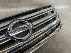 Close-up of the Nissan emblem on a chrome front grille of a car, showing horizontal chrome bars.