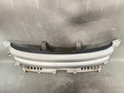 Grey automotive bumper component with two mounting brackets, lying on a scratched workshop surface.