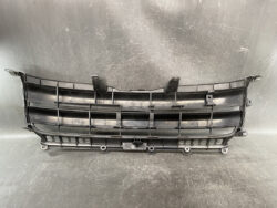 Black plastic car front grille with horizontal slats and mounting tabs, placed on a workshop table.