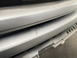 Close-up of a silver car front bumper with a thin scratch and minor scuffs near the grill area.