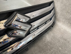 Close-up of a shiny chrome Suzuki emblem on a black front grille of a vehicle.
