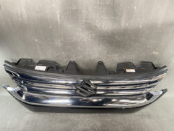 Front grille of a dark blue Suzuki with chrome horizontal bars and emblem in center.