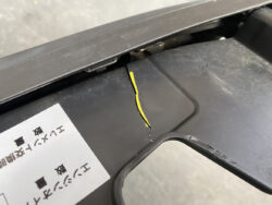 Close-up of a black plastic surface with a vertical crack exposing a yellow inner layer; a white label with Japanese text is visible nearby.