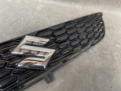 Close-up of a black honeycomb car grille with a chrome Suzuki 'S' emblem.