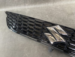 Close-up of a glossy black car grille with a chrome Suzuki emblem in the center.
