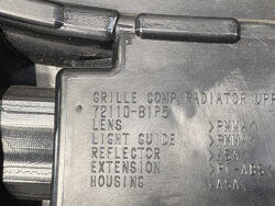 Close-up of a car headlight housing with embossed part description and material codes (PMMA, ASA).