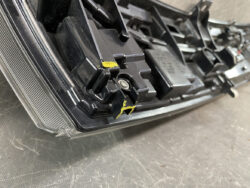 Close-up of a car headlight housing with yellow tape marks on the mounting bracket area.