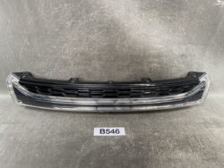 Car front grille with a honeycomb pattern and chrome trim laid on a gray workshop surface.