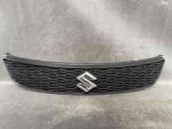 Black car front grille with a chrome Suzuki emblem in the center set on a textured surface