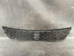 Black car front grille with hexagonal honeycomb pattern and a diamond-shaped emblem in the center on a dark background surface.