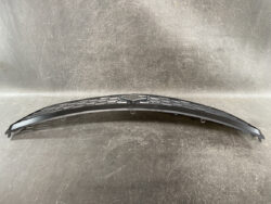 Curved black plastic car bumper grille with multiple mounting clips along the edge, photographed on a scratched metal surface.