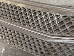Close-up of a dusty diamond-pattern car grille on a bumper area.