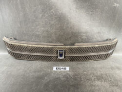 Front view of a car grille with diamond-pattern mesh and a central blue emblem on a grey surface