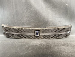 Front grille of a Toyota Voxy minivan with a diamond mesh pattern and central blue emblem.