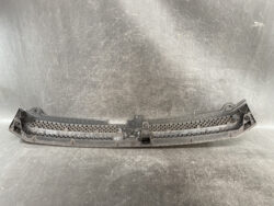 Plastic car bumper grille insert with mounting brackets and honeycomb mesh, dusty and used.