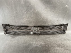 Long black car front grille with honeycomb mesh and central mounting area, laid flat on a workshop surface.