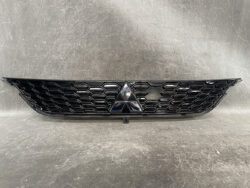 Black honeycomb front grille with a central Mitsubishi emblem on a dark surface, indicating a car's front fascia.