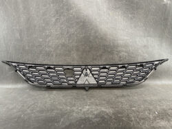 Front grille of a car with a black honeycomb mesh and a central triangular Mitsubishi emblem in the middle point of the grille's openings