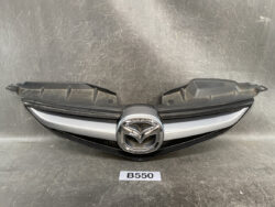 Front grille assembly with Mazda logo centered on a silver and black grille on a dark backdrop.