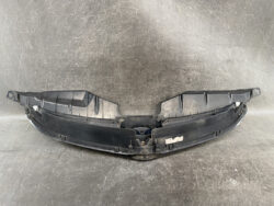 Black plastic car bumper component with mounting tabs laid on a workshop surface (front bumper area).