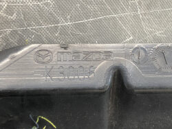 Close-up of a Mazda emblem with the model/code 'K3006' engraved on a textured gray metal surface.