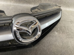 Close-up of a silver Mazda badge on the front grille of a car.