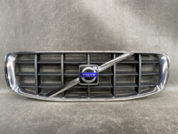 Front grille of a Volvo car featuring a chrome frame, black horizontal slats, and the blue Volvo emblem in the center with a diagonal chrome bar across it.