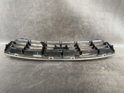 Long black plastic automotive panel with multiple shallow pockets, likely a car center console insert.