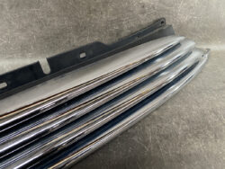 Chrome car bumper/grille trim with black mounting brace laid on a textured surface.