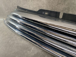 Chrome horizontal car grille slats stacked together with a black mounting bracket on top, resting on a textured surface.