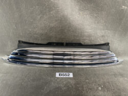 Chrome front bumper grille with black mounting bracket, laid on a workbench; part labeled B552 for automotive repair.