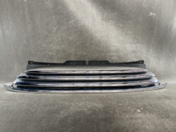 Chrome horizontal-bar car grille resting on a dark backing, photographed against a scratched metal backdrop