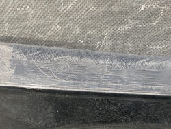 Close-up of a car door sill with the MINI emblem and the word 'GERMANY' embossed next to it, metal surface worn.