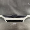 Front bumper section of a white car with a circular center grille and horizontal side vents against a dark backdrop.