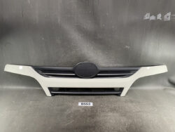 Front bumper section of a white car with a circular center grille and horizontal side vents against a dark backdrop.