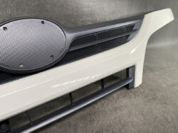 Close-up of a white car bumper with a large circular black speaker grille and horizontal vents.