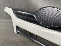 Front bumper of a white car featuring a black grille and a large round textured cover on the right side of the bumper