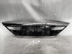 Black glossy car bumper with chrome trim resting on a workshop surface, showing the mounting recess in the center (rear bumper cover) used for a vehicle repair or replacement.