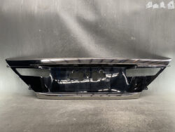 Glossy black car bumper with chrome trim, showing mounting points and a recessed area for the license plate across a workshop floor surface.