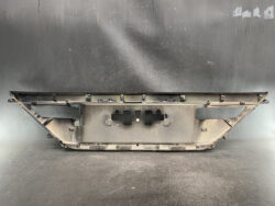 Rear view of a dusty car instrument cluster housing with mounting brackets on a dark surface.