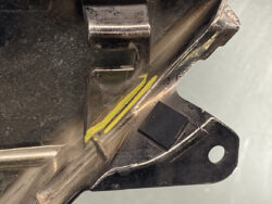 Close-up of a metal bracket with a yellow marker highlighting a crack along the edge.