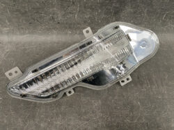 Clear plastic car taillight assembly with a curved lens resting on a dark workshop surface, showing internal reflectors.