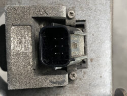 Dusty, six-pin rectangular electrical connector in a black plastic housing mounted in a dirty metal panel surface