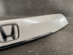Close-up of a silver car rear hatch with a chrome Honda emblem and trim piece below it.
