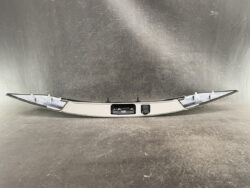 Curved car rear bumper piece laid flat, showing a central license-plate light housing and a small sensor area in the middle.